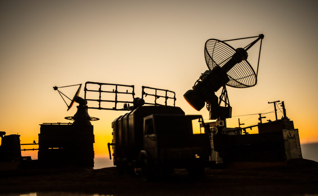 Silhouette of mobile air defense truck with radar antenna during sunset.